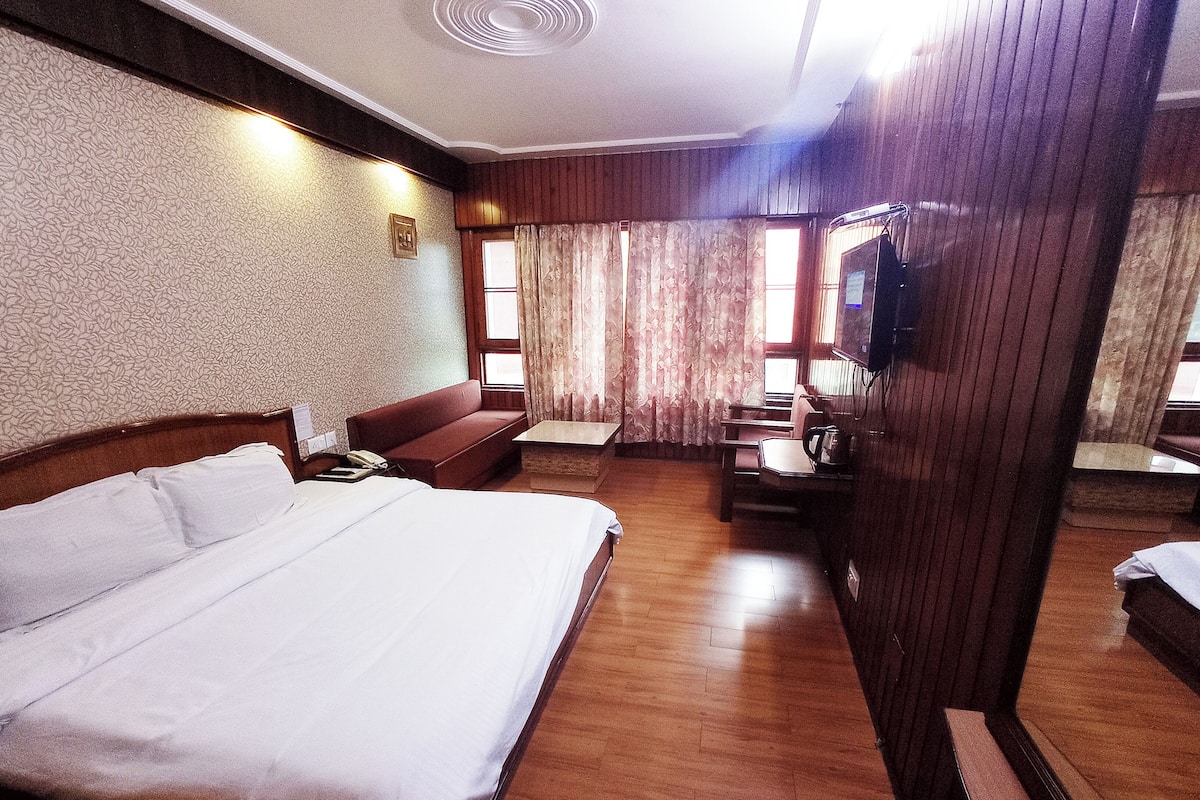 A hotel room with a large bed, a wooden desk, a sofa, and a television.