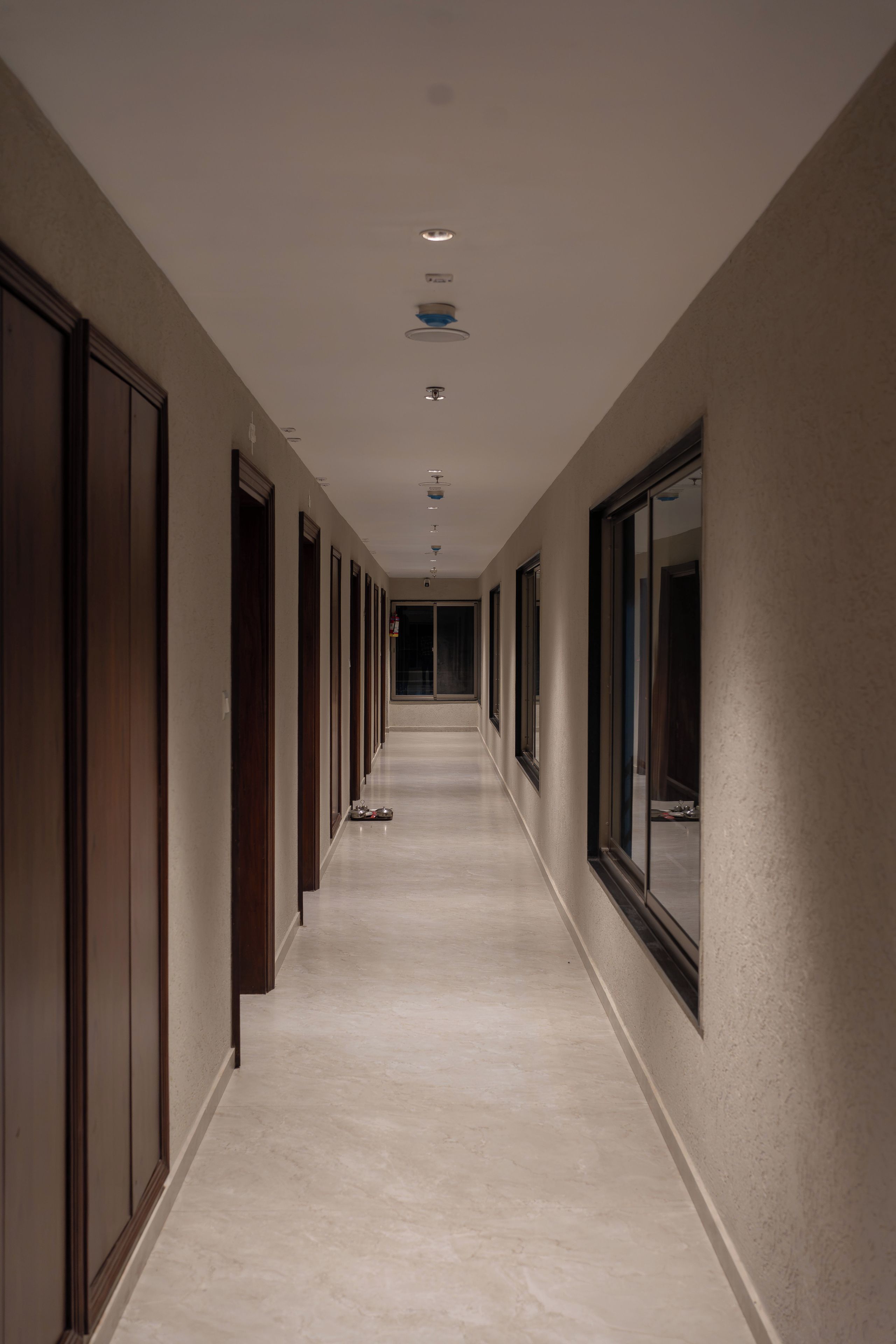 Un long couloir étroit, avec des portes de chaque côté, des luminaires encastrés et un sol carrelé.