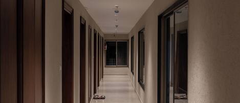 Un long couloir étroit, avec des portes de chaque côté, des luminaires encastrés et un sol carrelé.