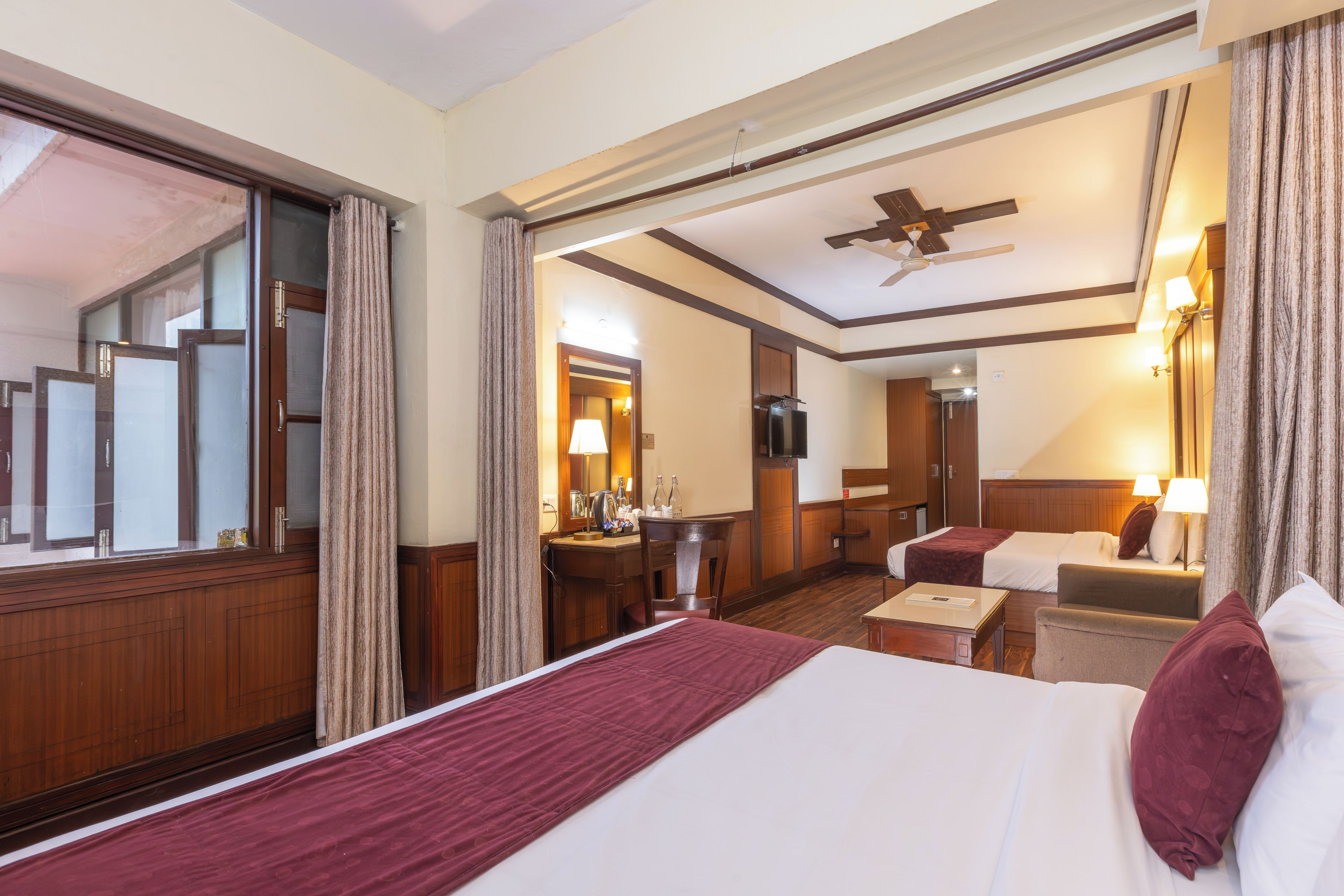 A hotel room with a large bed, a desk, a chair, a television, and a ceiling fan.