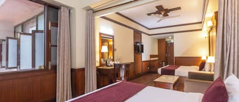 A hotel room with a large bed, a desk, a chair, a television, and a ceiling fan.