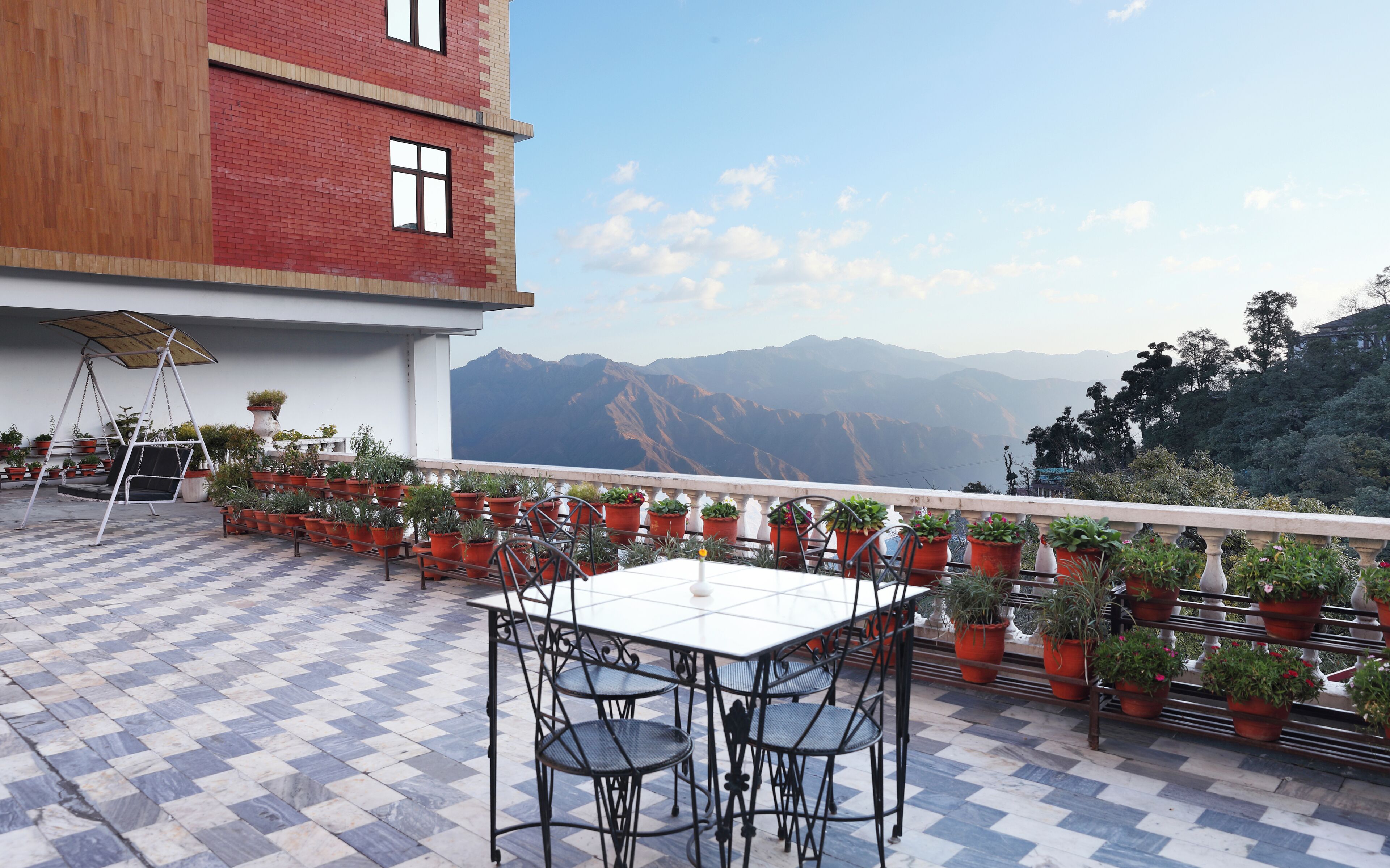 A terrace with a checkered floor, outdoor seating, potted plants, and a view of mountains.