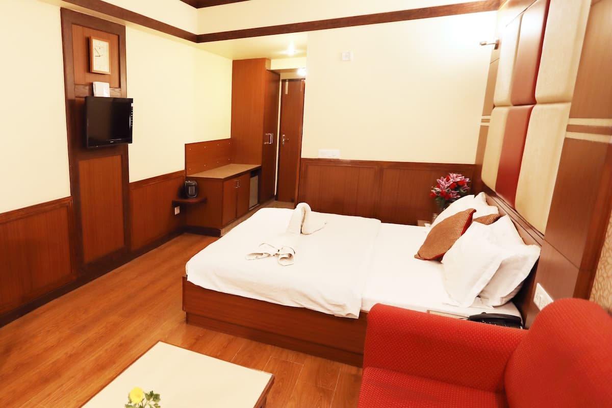 A hotel room with a bed, a red sofa, a small table with a vase, a TV, and a wooden wardrobe.