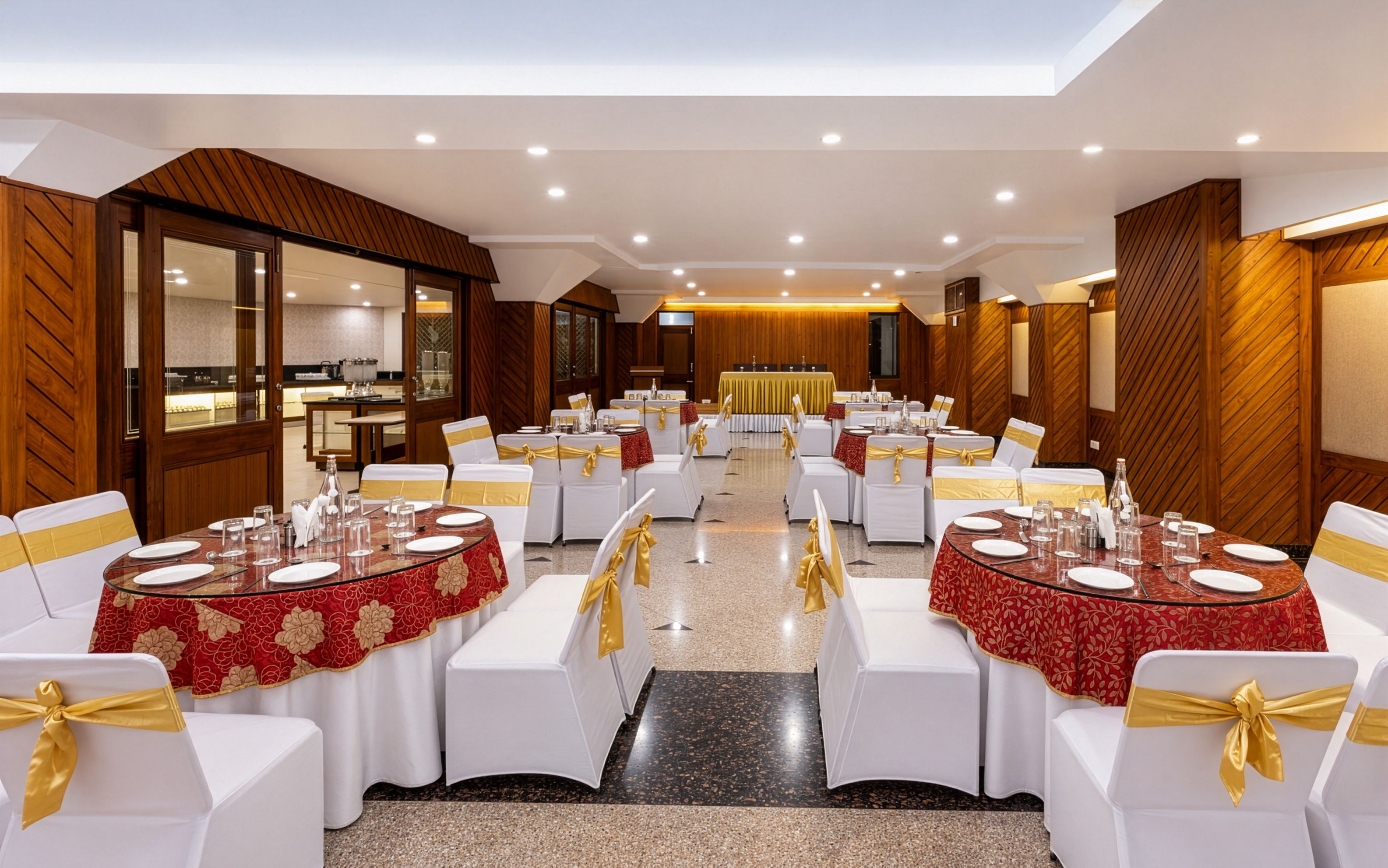 Un salón de banquetes con mesas redondas, sillas blancas y cintas doradas.