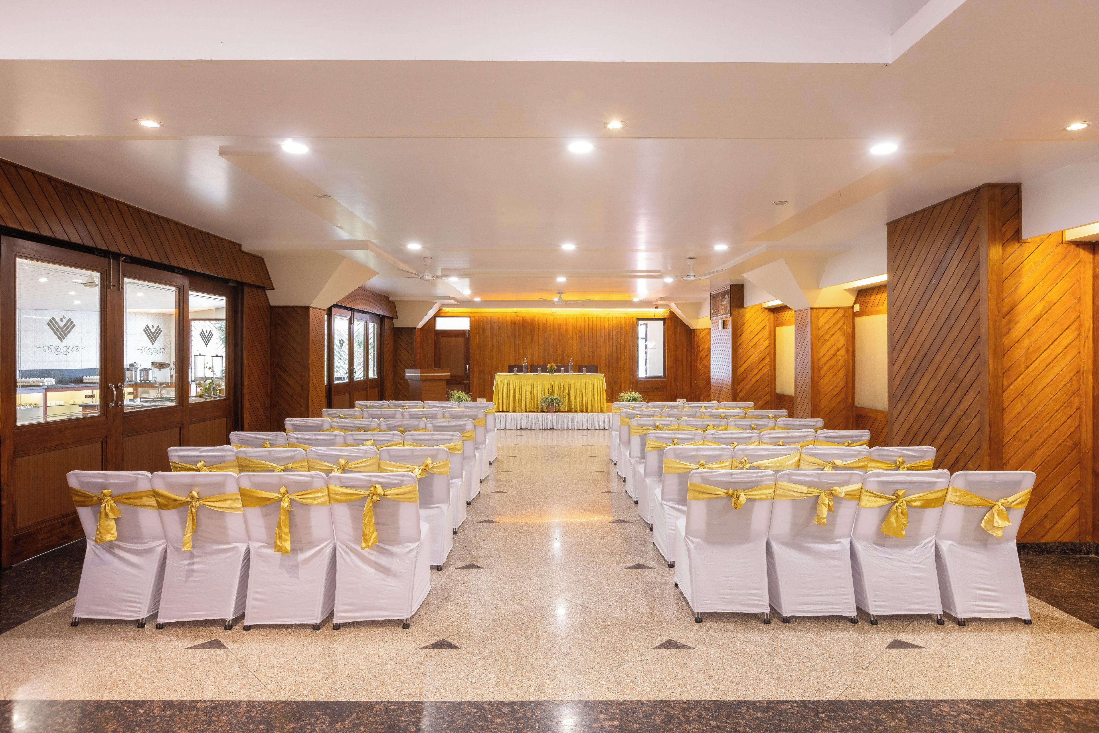 A conference room with rows of chairs, a stage with a yellow table, and wooden paneling on the walls.