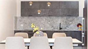 A modern kitchen with dark cabinets, a marble backsplash, and pendant lighting.