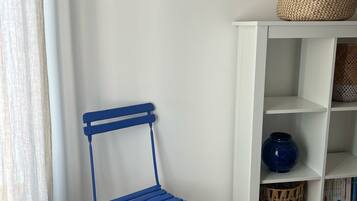 A room with a blue metal chair, a white shelf with baskets, and a wooden floor.