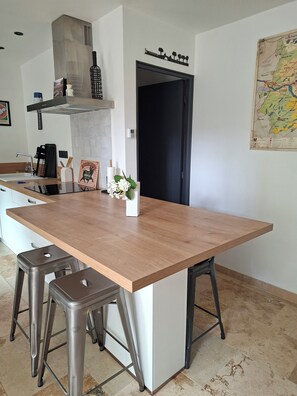 A modern kitchen with a large island, stainless steel stools, a black door, and a map on the wall.