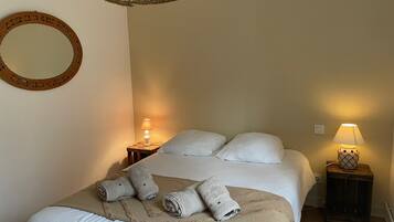 A neatly made bed with pillows and rolled towels, a round mirror, and two bedside lamps on wooden nightstands.