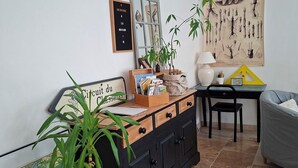 Ein Wohnzimmer mit einem schwarzen Schrank, einer Karte, einer Topfpflanze, einem Schreibtisch, einem Sessel und einer Wand mit einer botanischen Illustration.
