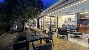Eine Außenpatio mit Esstisch und Stühlen, einer Couch und einer Küchenzeile mit Deckenventilator.