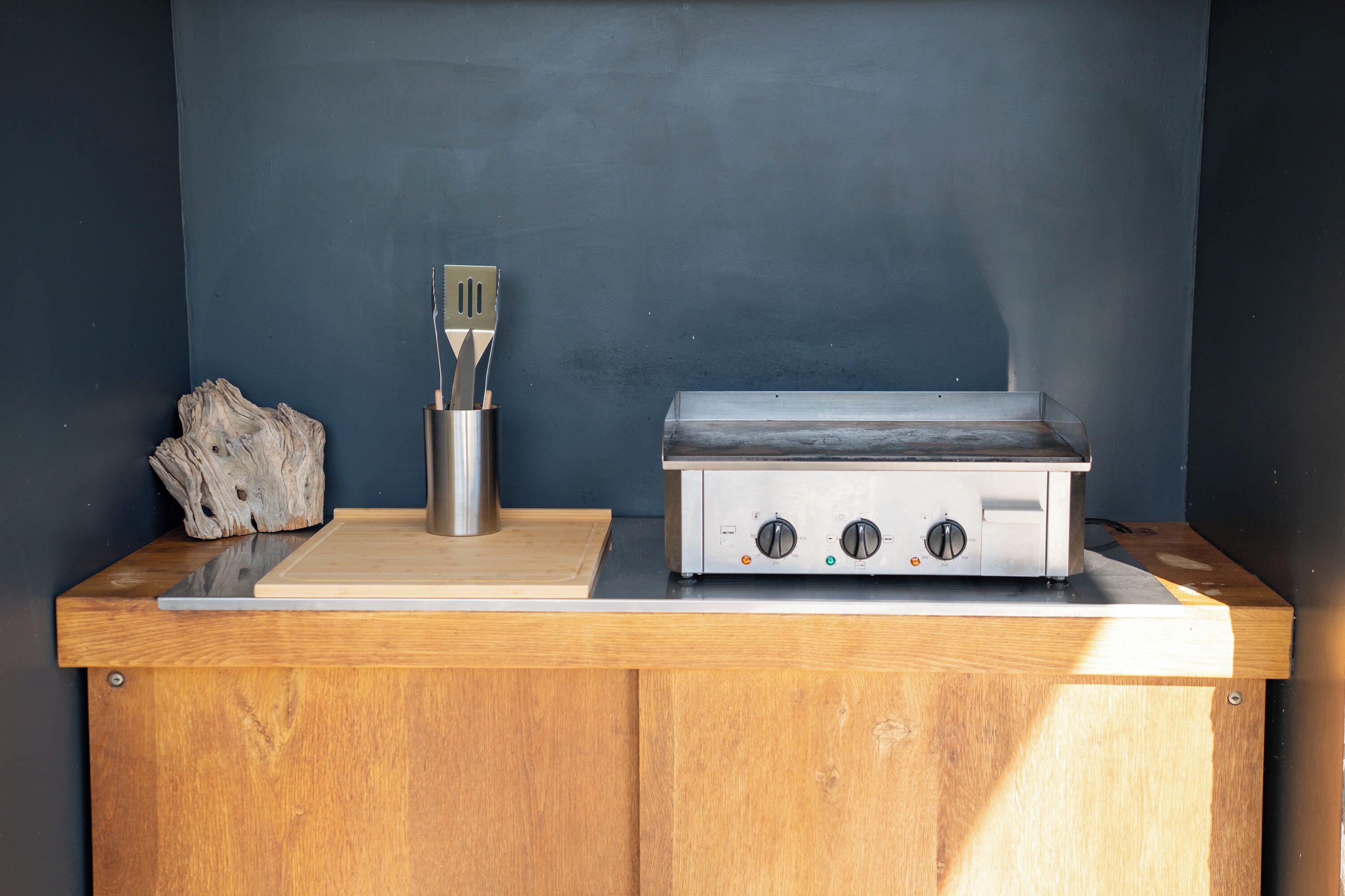 A kitchen with a stainless steel range hood, a wooden countertop, and a piece of driftwood.