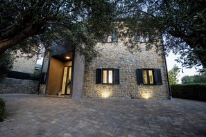 A stone building with two windows and a door, surrounded by trees and a paved area. - Villa Picholine (Novalja)