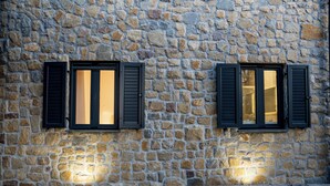 Ein Steinhaus mit zwei Fenstern, jeweils mit dunklen Fensterläden.