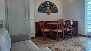 Een woonkamer met een grijze bank, een eettafel met houten stoelen, en een decoratief schilderij aan de muur.