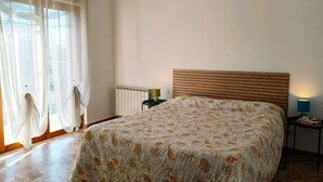 Een slaapkamer met een bed, nachtkastje, lamp en een raam met gordijnen.