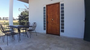 Een overdekt terras met een tafel en stoelen, een houten deur en uitzicht op het buitengebied.