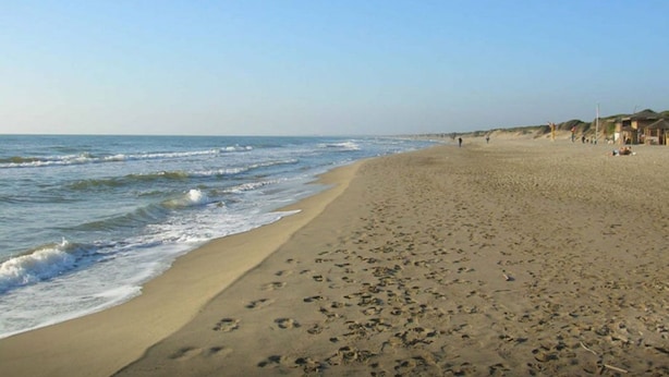 Een strand met voetafdrukken die naar een gebouw met meerdere daken leiden.