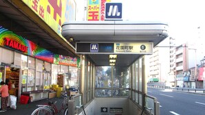 Katettu bussipysäkki, jossa on kyltti, josta käy ilmi, että pysäkki on Hanazokon aseman lähellä.