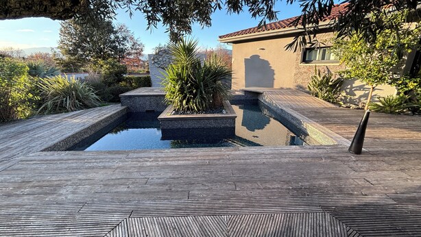 A swimming pool with a wooden deck, surrounded by plants and a stone wall. - Maison T2 Casa Alegria Peace and greenery in the heart of the Pyrénées-Orientales  (Joch)