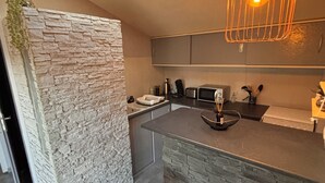 A modern kitchen with a stone accent wall, a skylight, and a central island with bar stools. - Maison T2 Casa Alegria Peace and greenery in the heart of the Pyrénées-Orientales  (Joch)