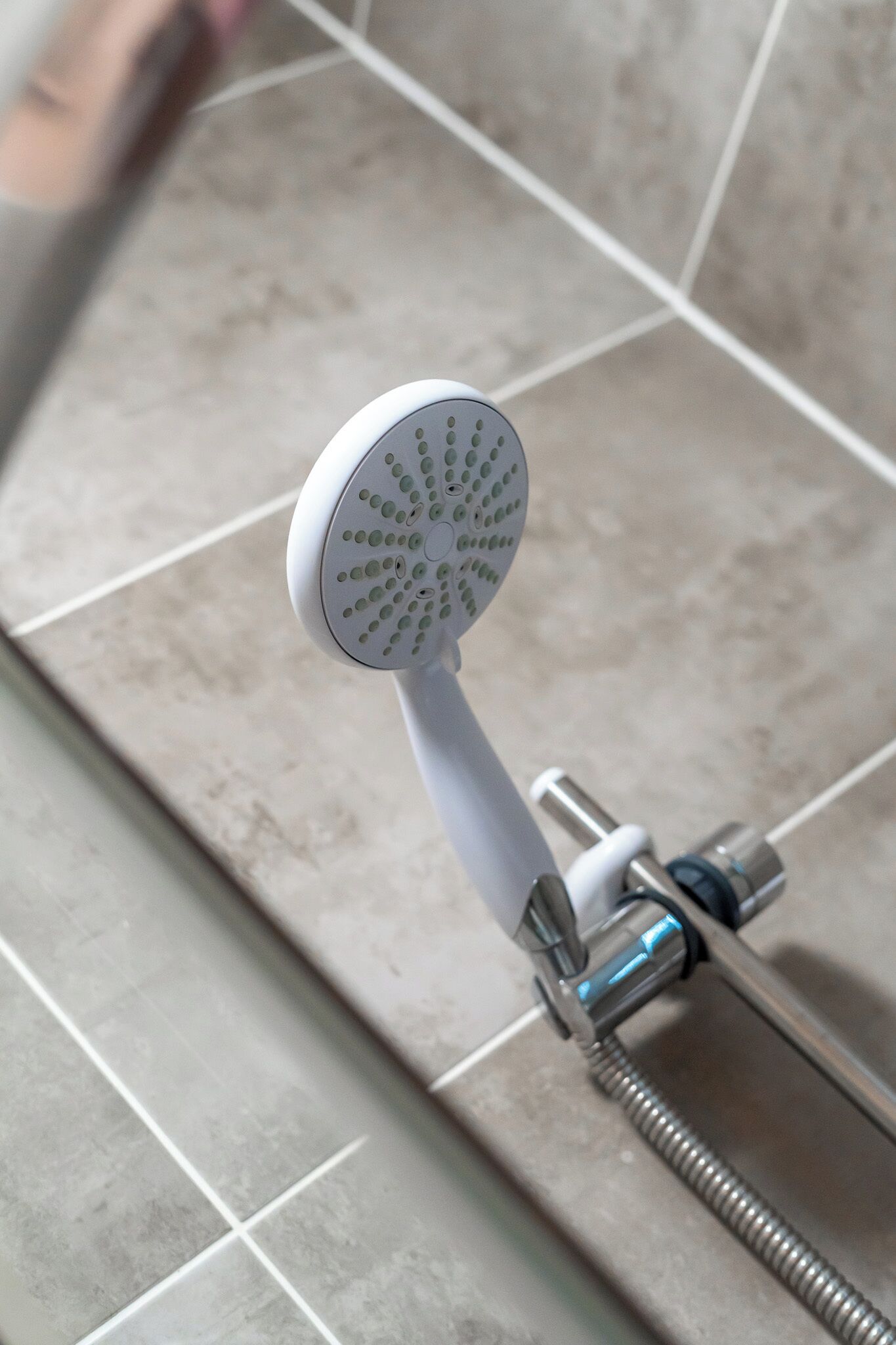 Un pommeau de douche de forme ronde et perforée, fixé à un tuyau métallique par un flexible.