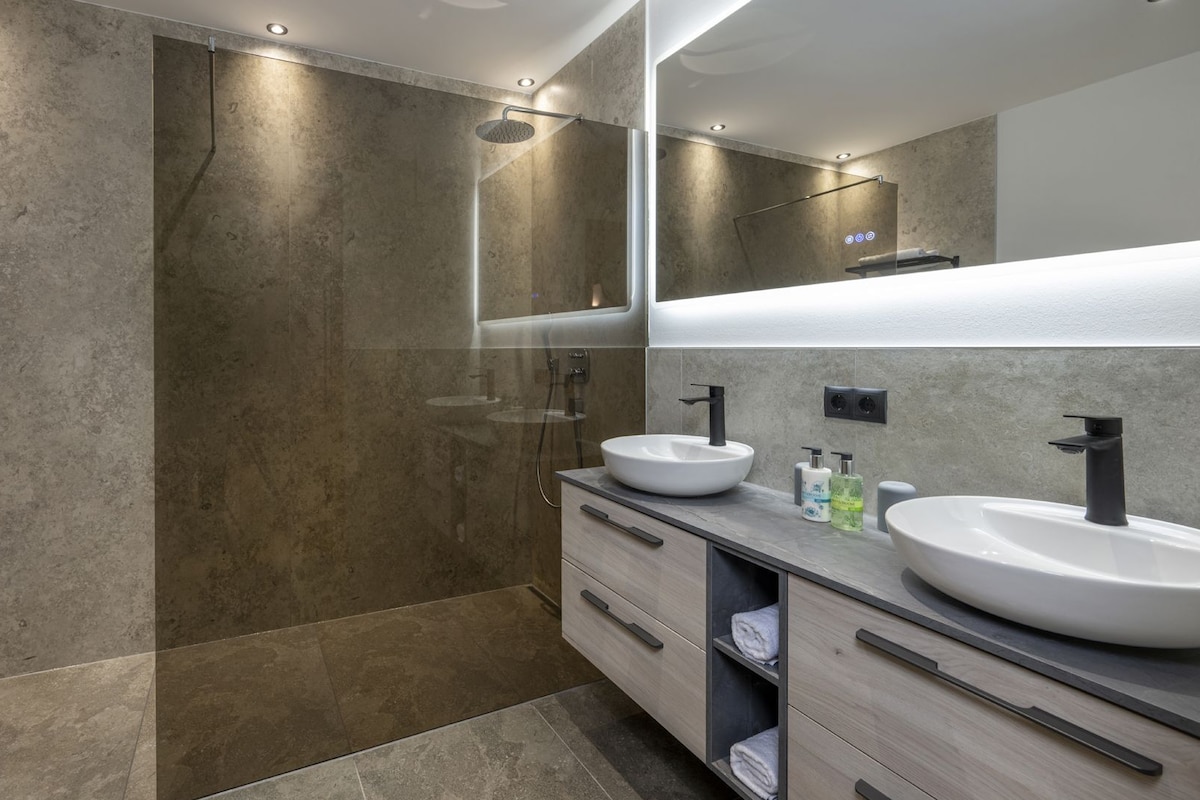 Une salle de bain moderne avec deux lavabos, une douche et un grand miroir.