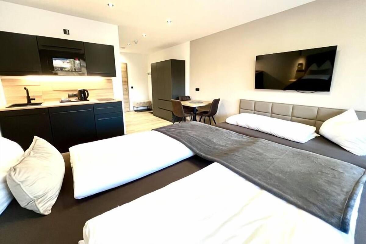 A hotel room with two beds, a desk, a TV, and a kitchenette.