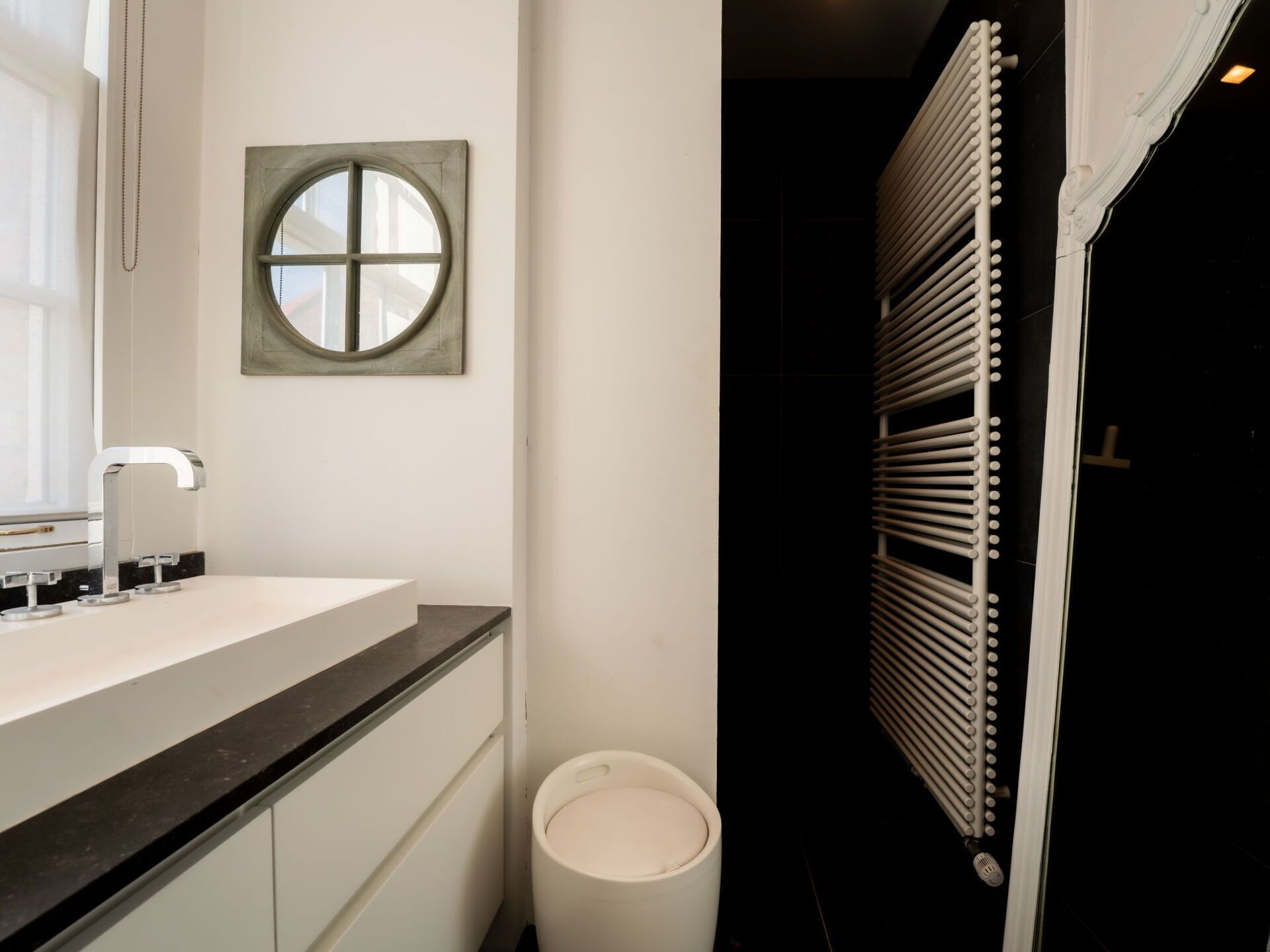 Ein Badezimmer mit einem weißen Waschbecken, einem runden Spiegel und einer weißen Toilette.