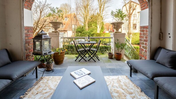 A covered patio with a brick archway, outdoor seating, and potted plants.