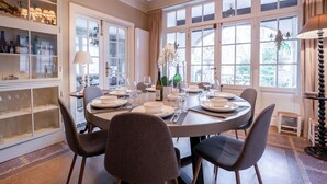 A dining room with a round table set for four, surrounded by chairs. There are glass cabinets with decorative items and a chandelier above the table.