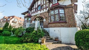 A two-story house with a prominent bay window, a brick facade, and a well-maintained garden with a paved entrance.