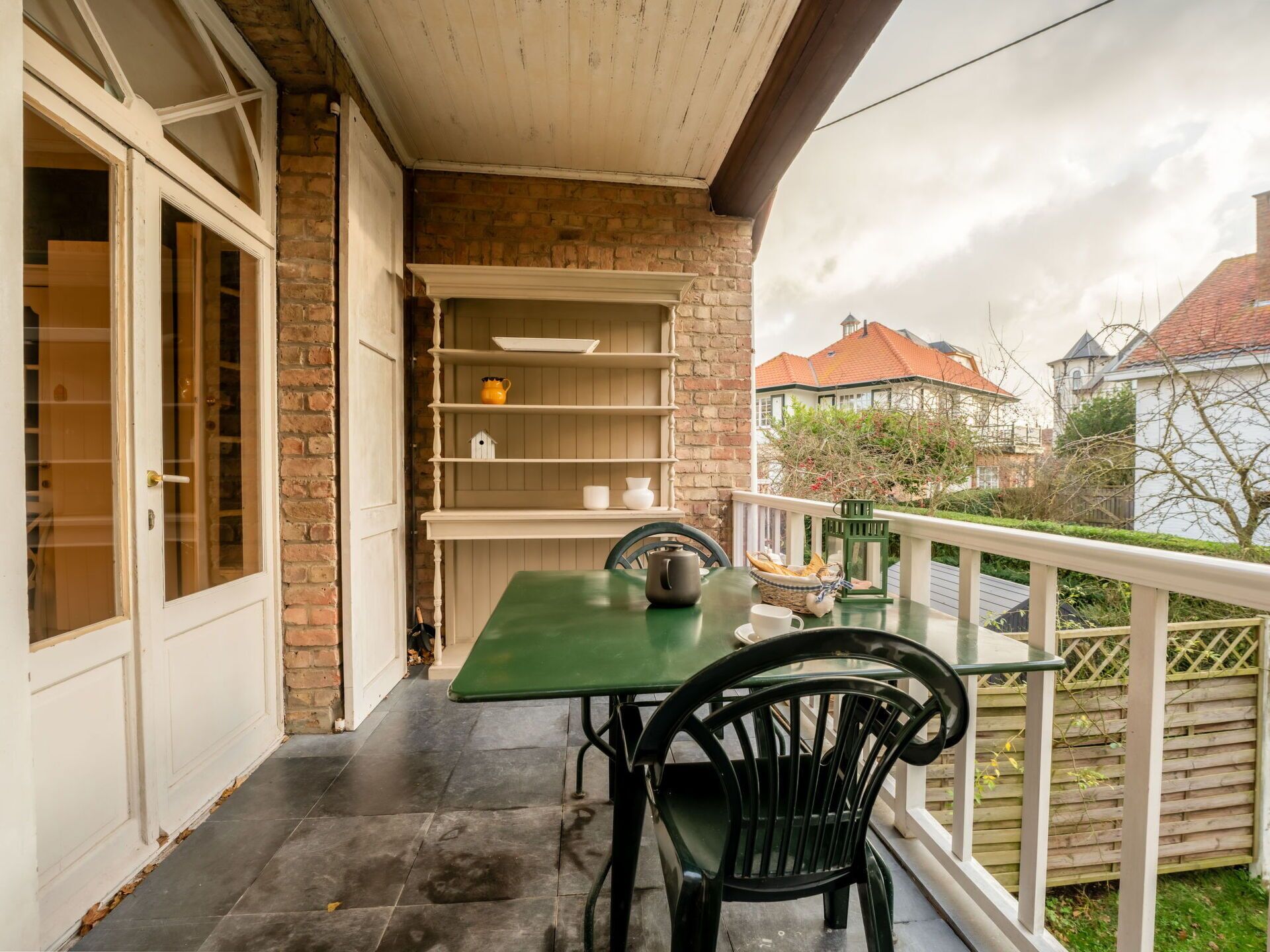 A balcony with a green table and black chairs, a white door, and a brick wall.