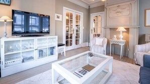 A living room with a television, glass cabinet, white armchair, and a glass coffee table.