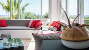 Een moderne woonkamer met een bank, rode en witte kussens, een kleine tafel met een lamp en een potplant.