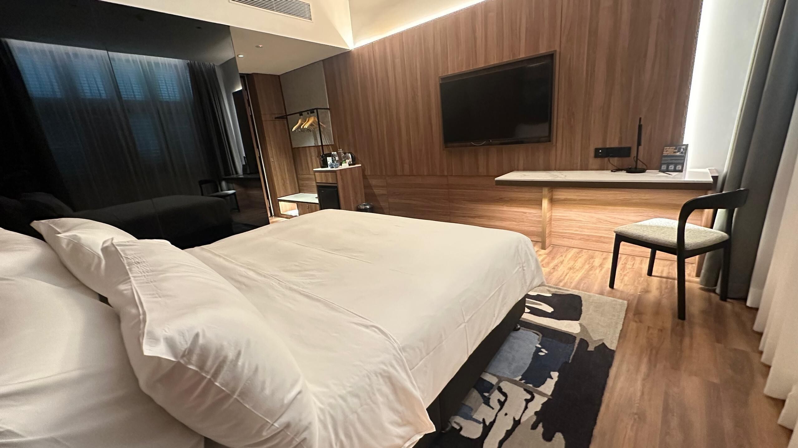 A hotel room with a large bed, a desk, a chair, and a TV on the wall.