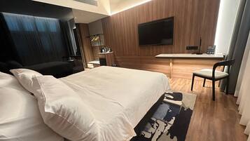 A hotel room with a large bed, a desk, a chair, and a TV on the wall.