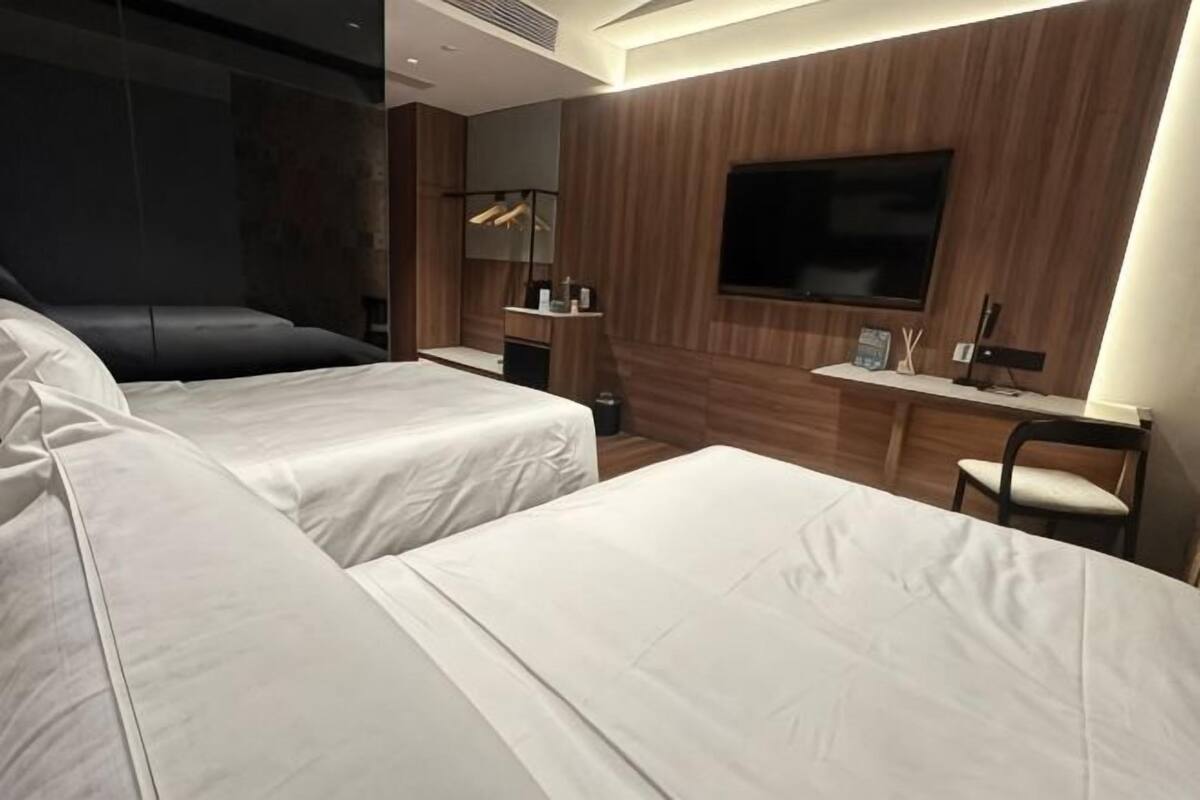 Ein Hotelzimmer mit zwei Betten, einem Schreibtisch, einem Stuhl, einem Fernseher und einem Spiegel.