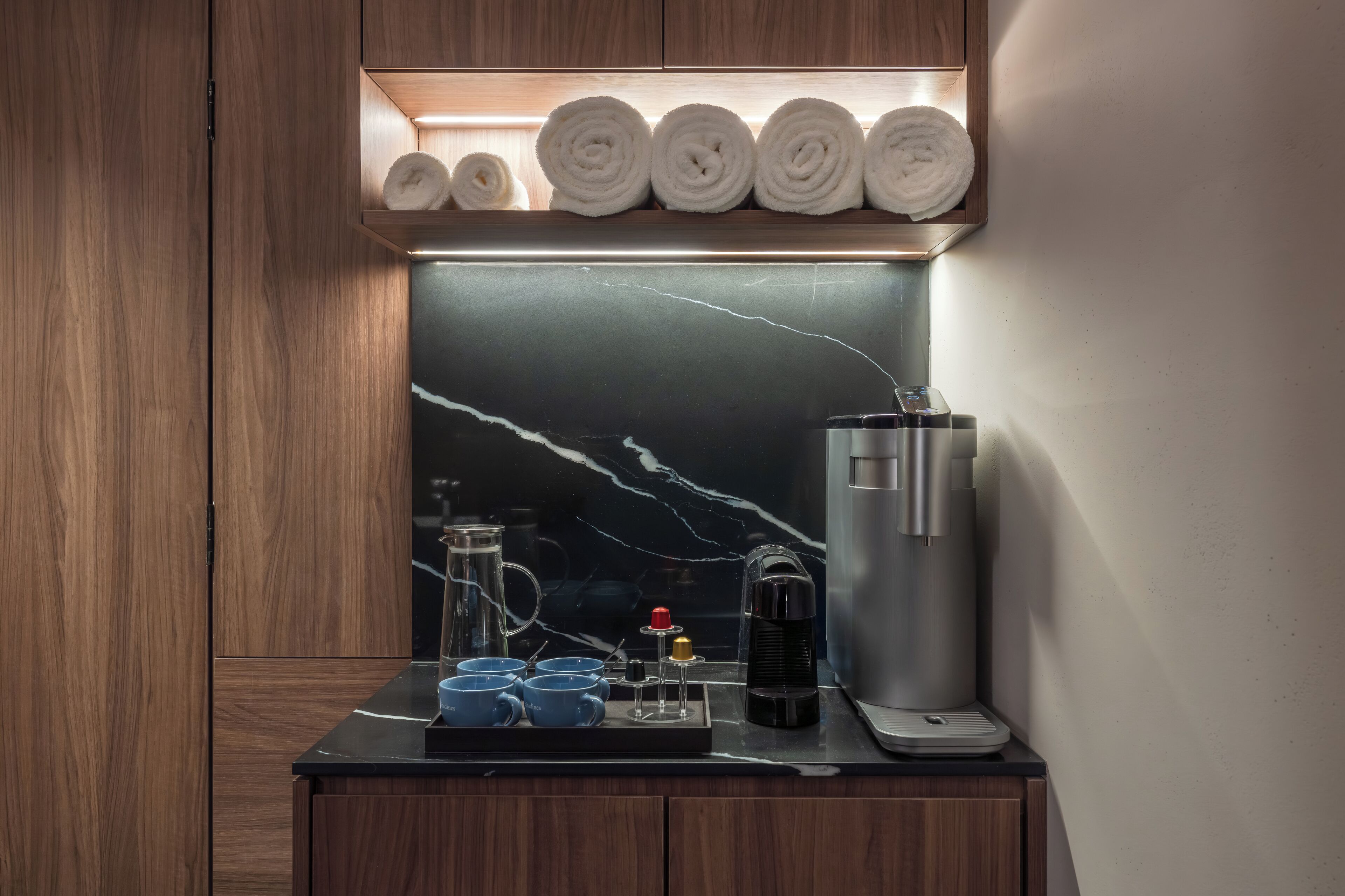 Ein modernes Badezimmer mit Marmorplatte, einer Kaffeemaschine und ordentlich gerollten Handtüchern auf einem Regal.
