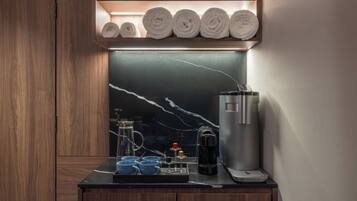 Ein modernes Badezimmer mit Marmorplatte, einer Kaffeemaschine und ordentlich gerollten Handtüchern auf einem Regal.
