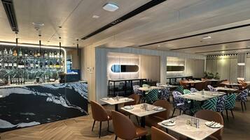 A modern restaurant with a bar area, wooden flooring, and tables with patterned cushions.