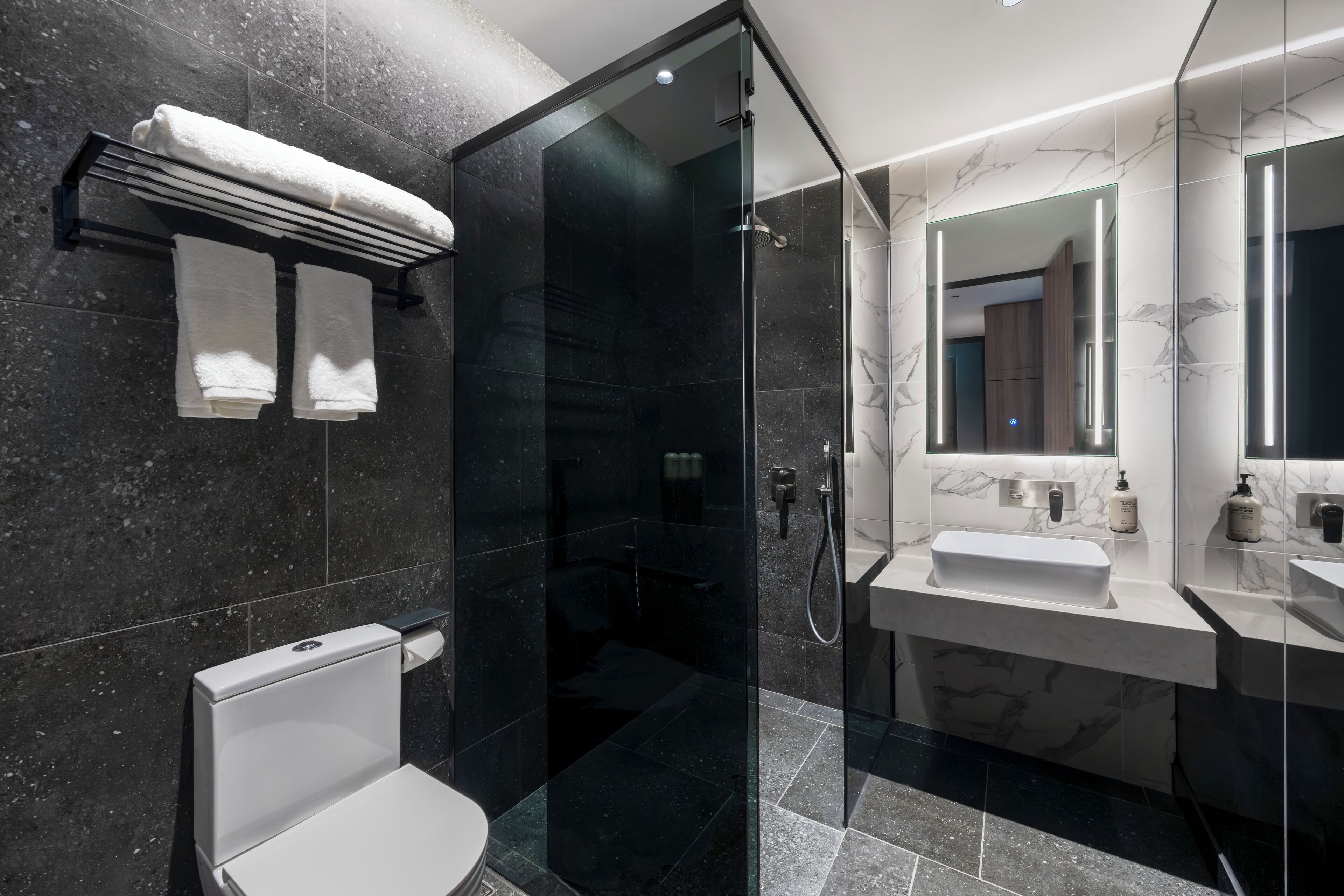 A modern bathroom with a glass-enclosed shower, a white toilet, and a vanity with a mirror.