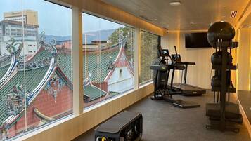 A modern gym with exercise equipment, large windows with a view of traditional architecture, and a ceiling with recessed lighting.