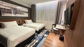 Hotelkamer met twee bedden, een bureau, een stoel, een televisie en een groot raam met gordijnen.