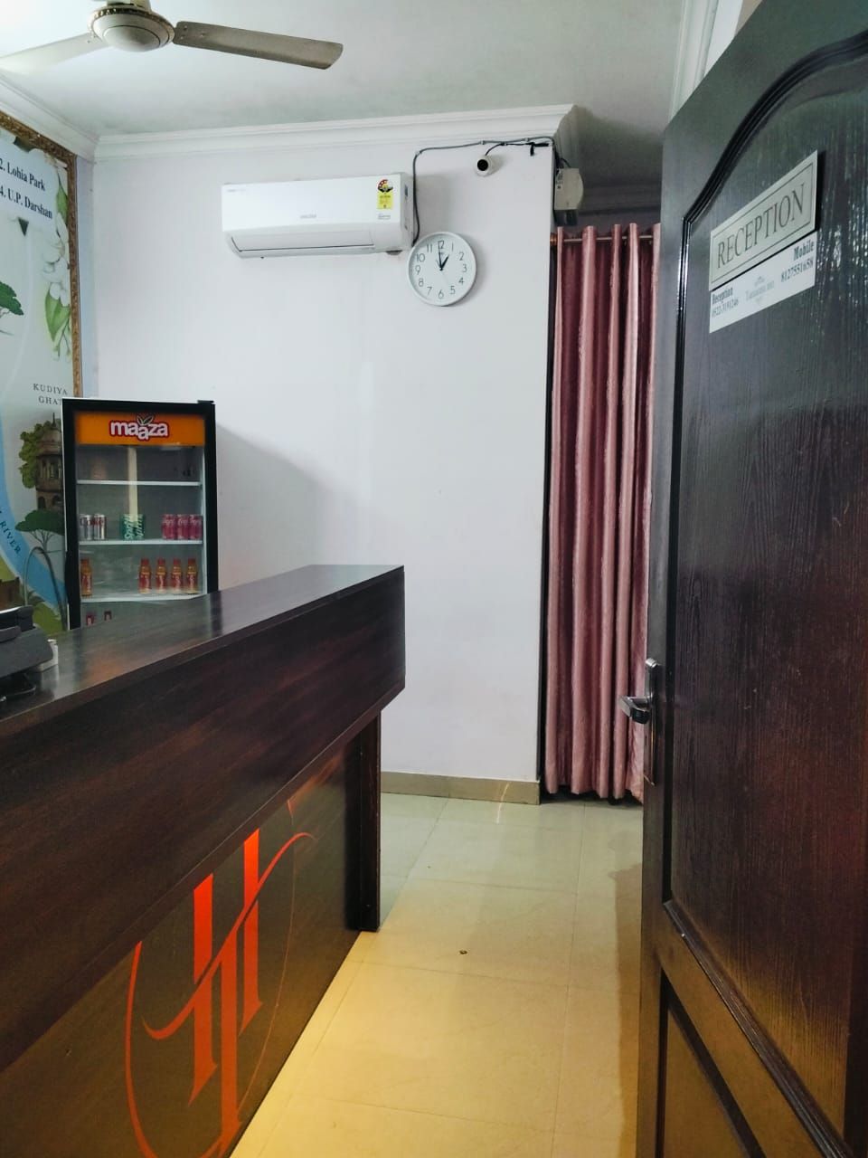 A reception area with a reception desk, a clock, an air conditioning unit, and a refrigerator.