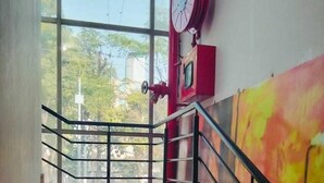 Uma escadaria com corrimão de metal que leva a um quarto com uma janela grande e um carretel de mangueira de incêndio vermelho.