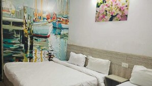 Quarto de hotel com duas camas, uma grande pintura de barcos na parede e uma obra de arte floral sobre a cama.