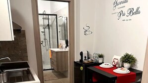Cocina compacta con zona de comedor, mostrando una mesa para dos en rojo y negro, una cafetera y una planta en maceta.
