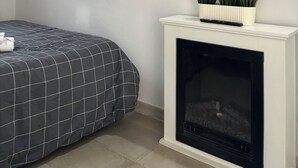 Un dormitorio con una cama, televisión montada, chimenea y una planta en maceta.