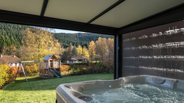 A hot tub with a view of a playground and a forested hill. - 
Maéva's Chalet: Jacuzzi and Terrace. (Xonrupt-Longemer)